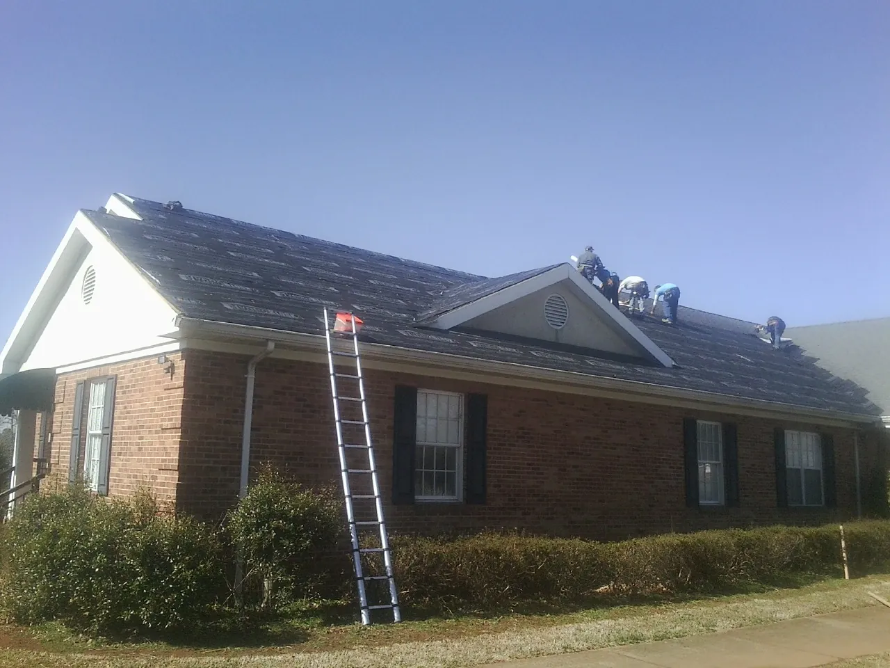 Crew tearing shingles off a brick ranch roof with a ladder set — Emergency Roof Repair work by our crew in Neosho