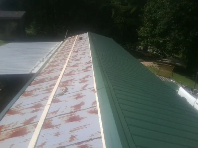 Old rusted panels beside newly installed green metal roofing — Wind Damage Roof Repair by Roofing Brothers in Neosho