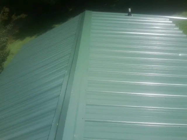 New green metal panels meeting at the ridge of a roof — Flat Roof Repair work by our crew in Neosho