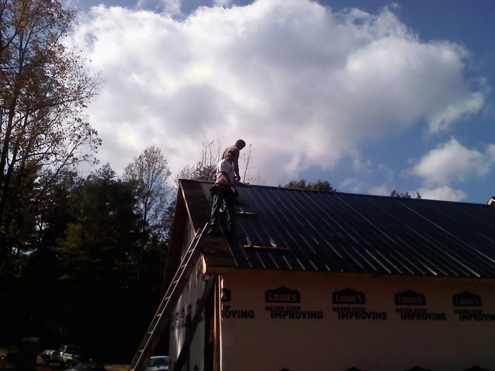 Roofer fastening dark metal panels high against a cloudy sky, from a Roof Inspection job in Neosho