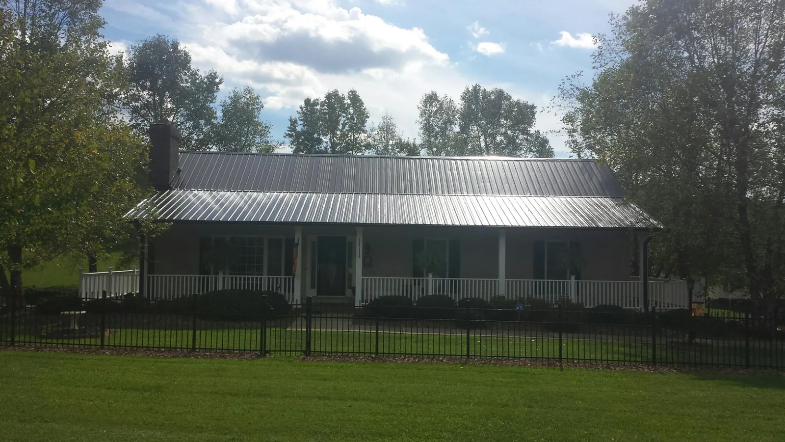 Gray metal roof on a brick ranch with a full width front porch — Gutter Guard Installation work by our crew in Neosho