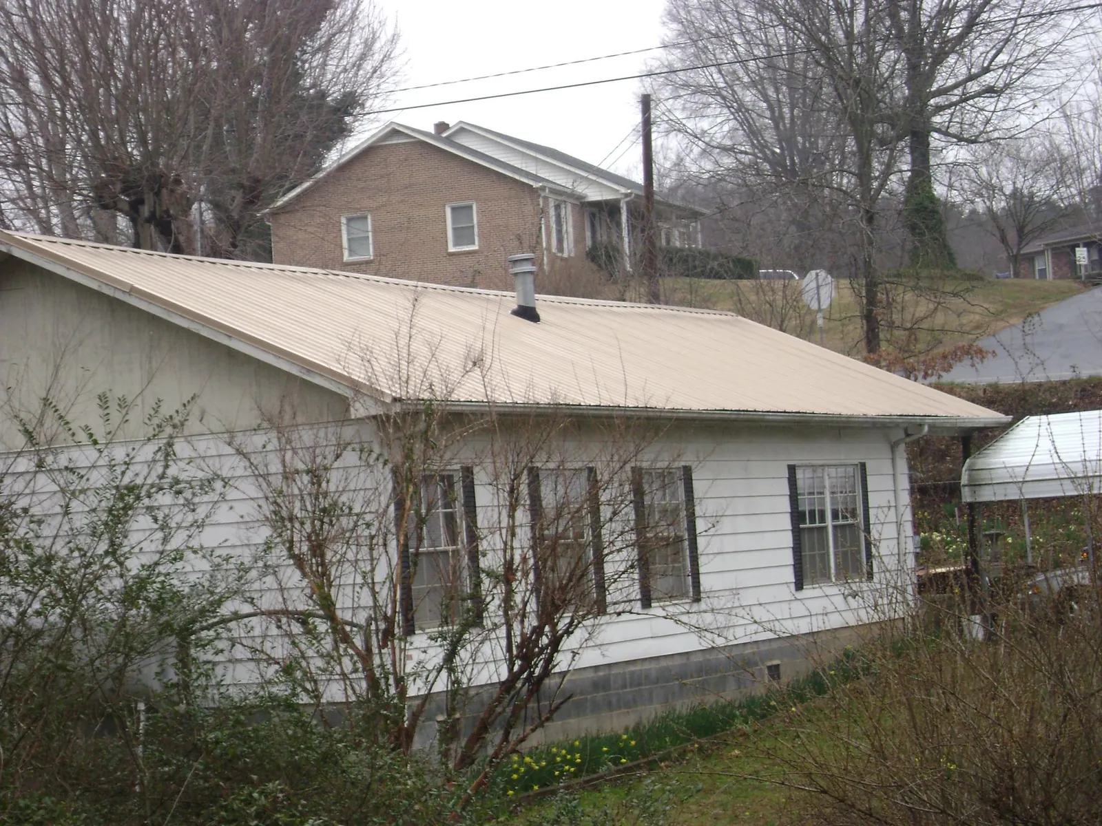 Tan metal roof on a white sided house set into a hillside — Commercial Roofing by Roofing Brothers in Neosho