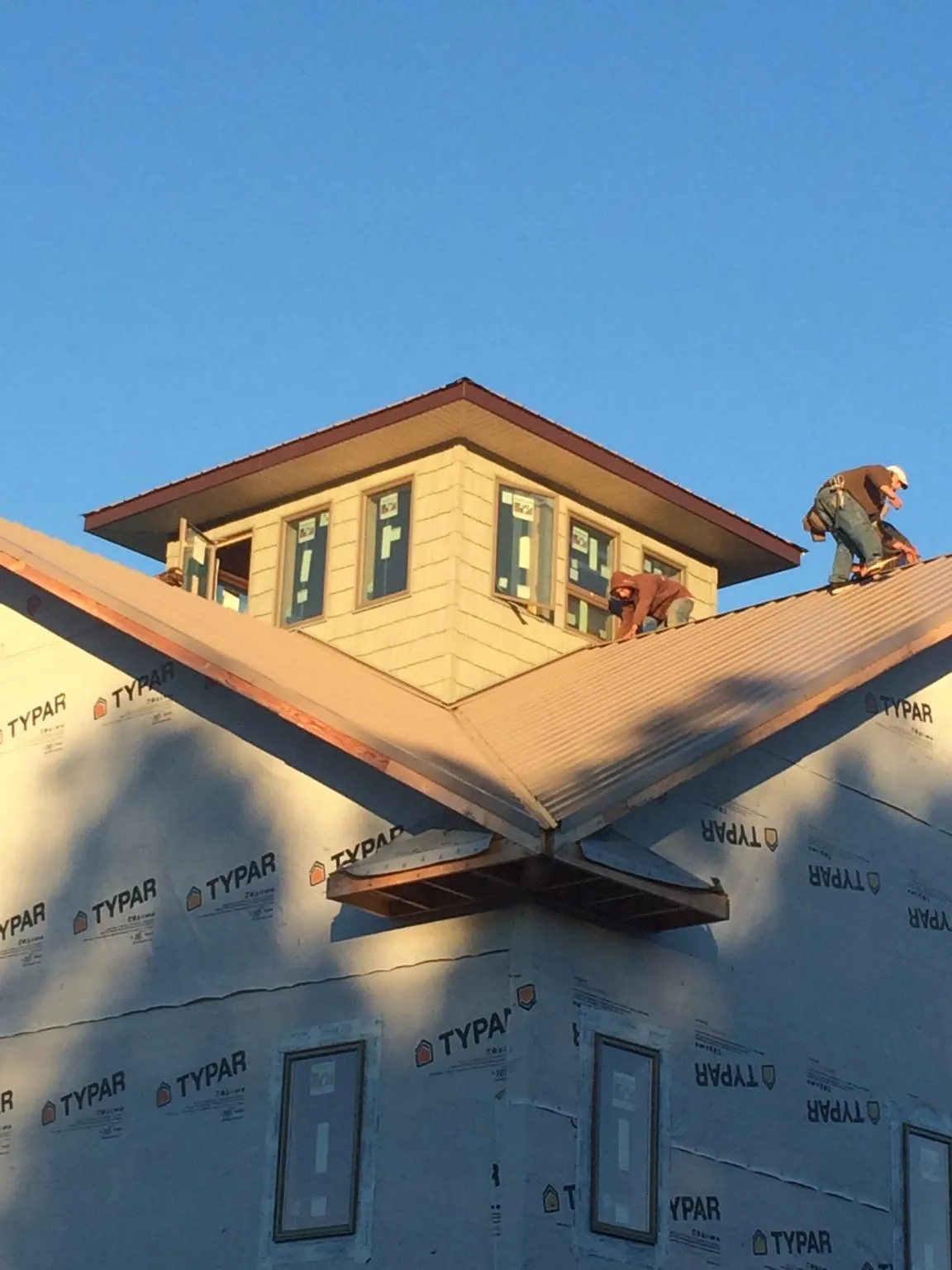 Roofers working around a rooftop cupola on a new metal roof at sunset — Roof Waterproofing in Neosho by Roofing Brothers